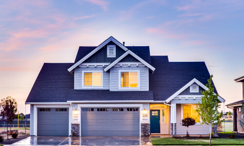 A nice suburban house with nice garage doors lighted up near sunset